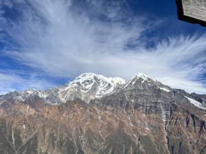 A wide view of the snow-capped Mardi Himal mountains beneath a clear blue sky, with soft clouds drifting above.