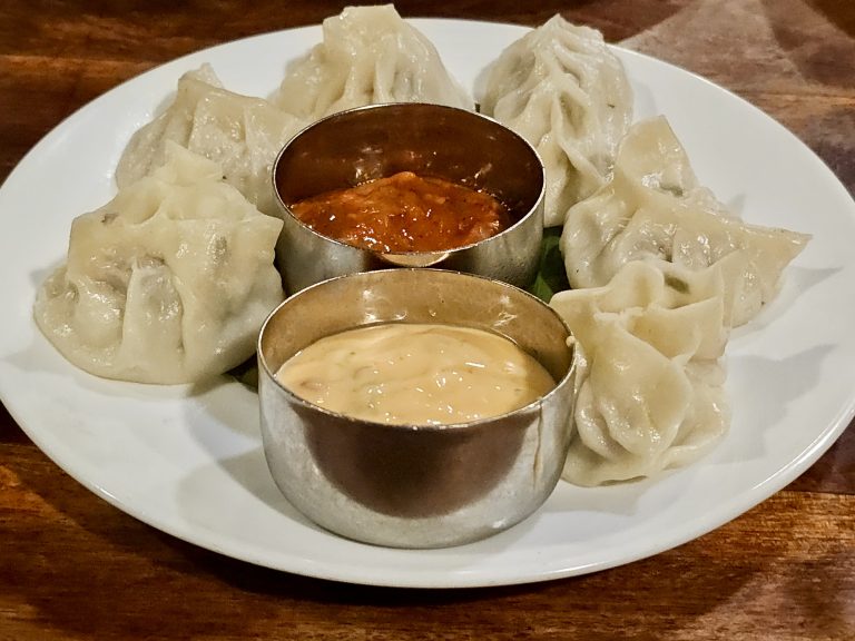 A plate of steamed chicken momos served with red and pink sauces