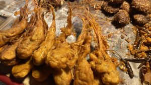 A close-up of golden-brown fried prawns served on a newspaper, with fried chilies and onions beside them, capturing a vibrant street food vibe.