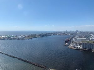 A wide view of a calm harbor with industrial tanks and buildings along the waterfront, seen from Chiba Port Tower over Tokyo Bay.