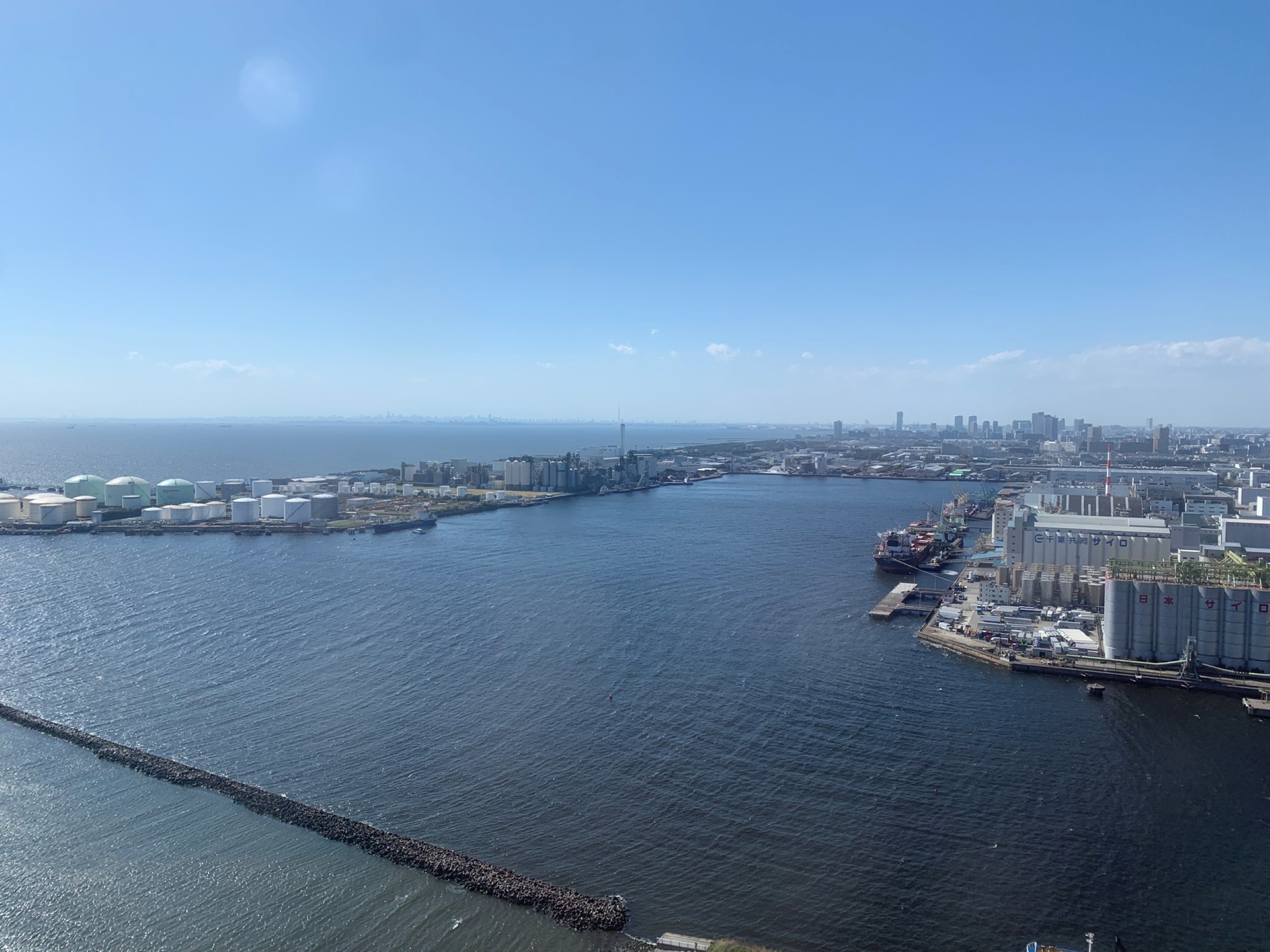 A wide view of a calm harbor with industrial tanks and buildings along the waterfront, seen from Chiba Port Tower over Tokyo Bay.