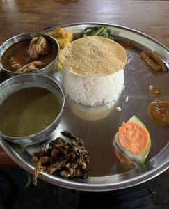 A traditional Nepali khana set served on a steel plate with rice, curry, lentils, vegetables, pickles, and sides.