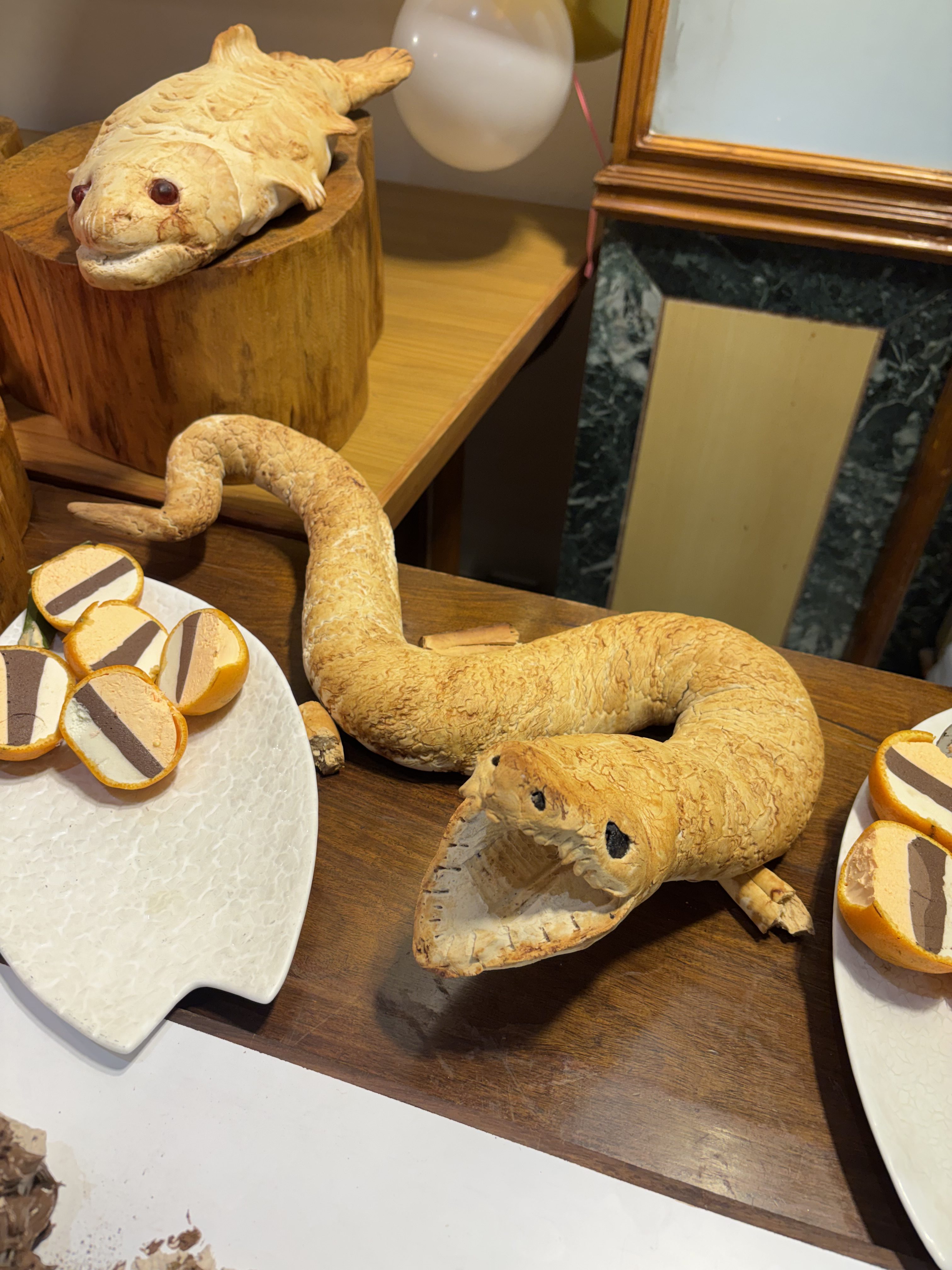 A display featuring intricate edible sculptures resembling a fish and a snake, crafted from a light-colored dough.