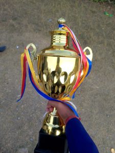 
A person holding a shiny gold trophy adorned with colorful ribbons. 