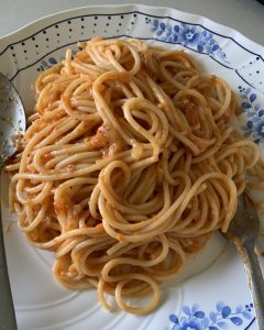 A plate of spaghetti is piled high, coated in a rich, reddish sauce. The dish is served on a white plate with a blue floral design. 
