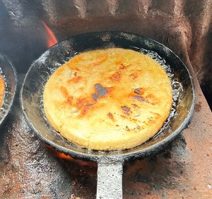 A close-up view of a round, golden-brown tortilla frying in black pans over a heat source.