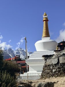 A large white stupa with a striped golden dome is prominently featured in the foreground, surrounded by rocky terrain.
