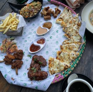 A colourful food platter with fries, salad, spring rolls, fried chicken, glazed chicken with sauces, and cheesy flatbread. 