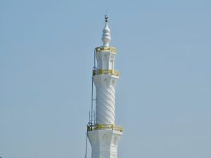 A tall white mosque minaret rises against a clear blue sky in Vazhakkad, Malappuram, with clean lines and peaceful surroundings. 