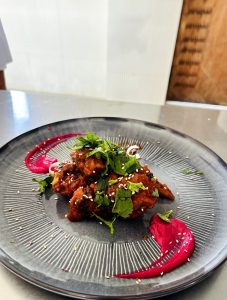 Chicken chilli served on a dark gray plate, topped with herbs and sesame seeds.