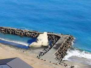 Aerial view of a coastal area featuring a stone jetty extending into the turquoise-blue ocean.