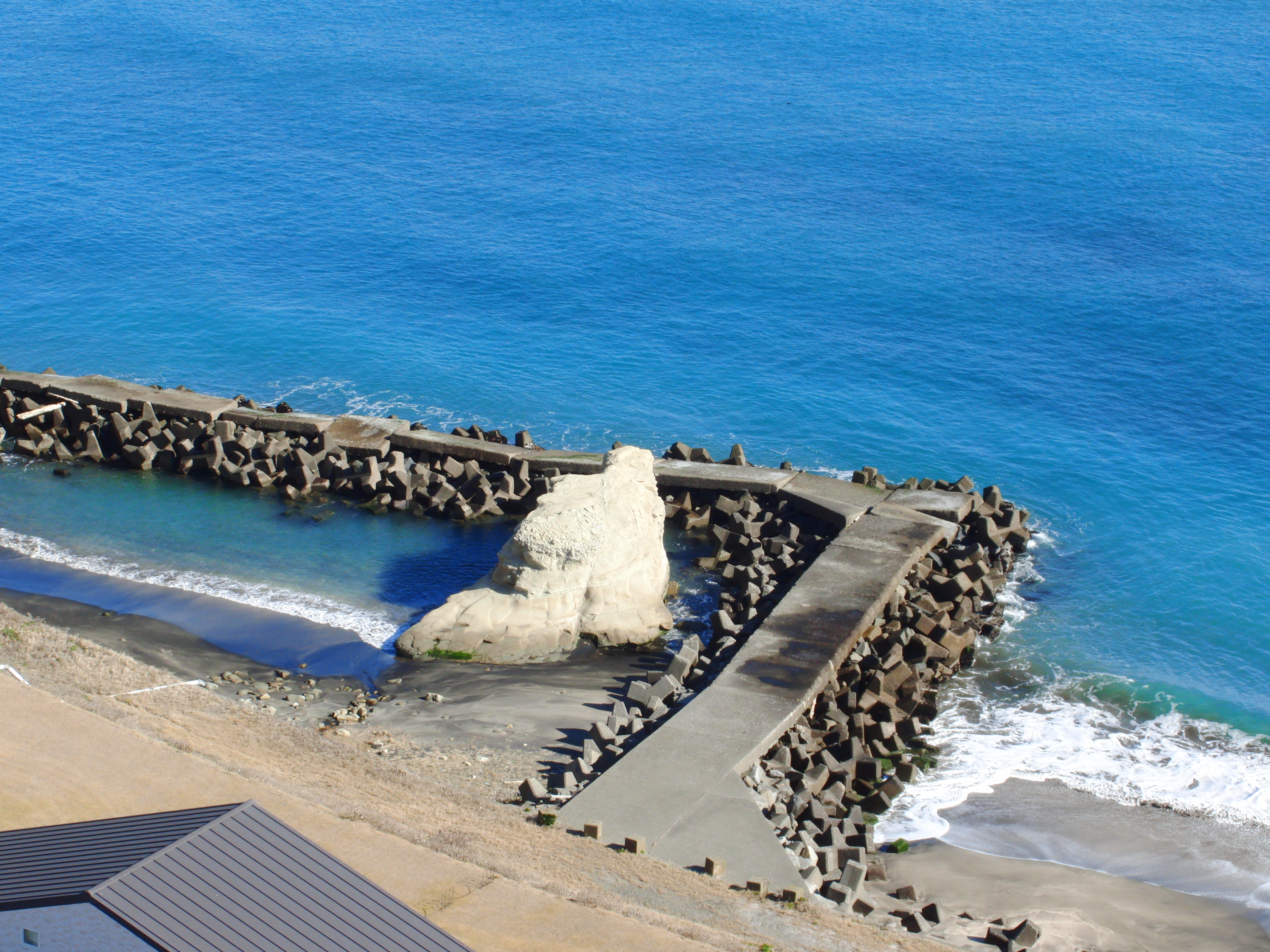 Aerial view of a coastal area featuring a stone jetty extending into the turquoise-blue ocean.