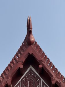 The ornate red peak of a traditional roof with intricate carvings and a bird-shaped finial against a clear blue sky.
