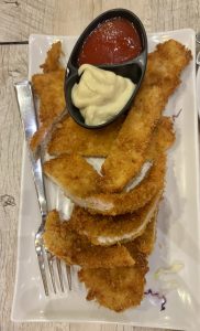 A plate of golden-brown breaded chicken strips arranged neatly, accompanied by a small black dish containing ketchup and mayonnaise.