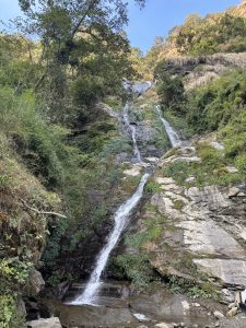A cascading waterfall flows down a rocky cliff, surrounded by lush greenery.