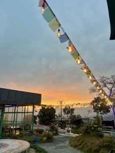 A serene outdoor scene at sunset, featuring a colorful string of lights and prayer flags draped across the sky.