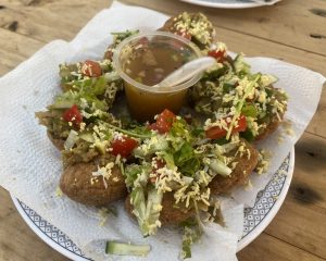 A plate of stuffed, crispy puris topped with vegetables and cheese, surrounding a cup of tamarind sauce. Vibrant, inviting, and ready to eat.