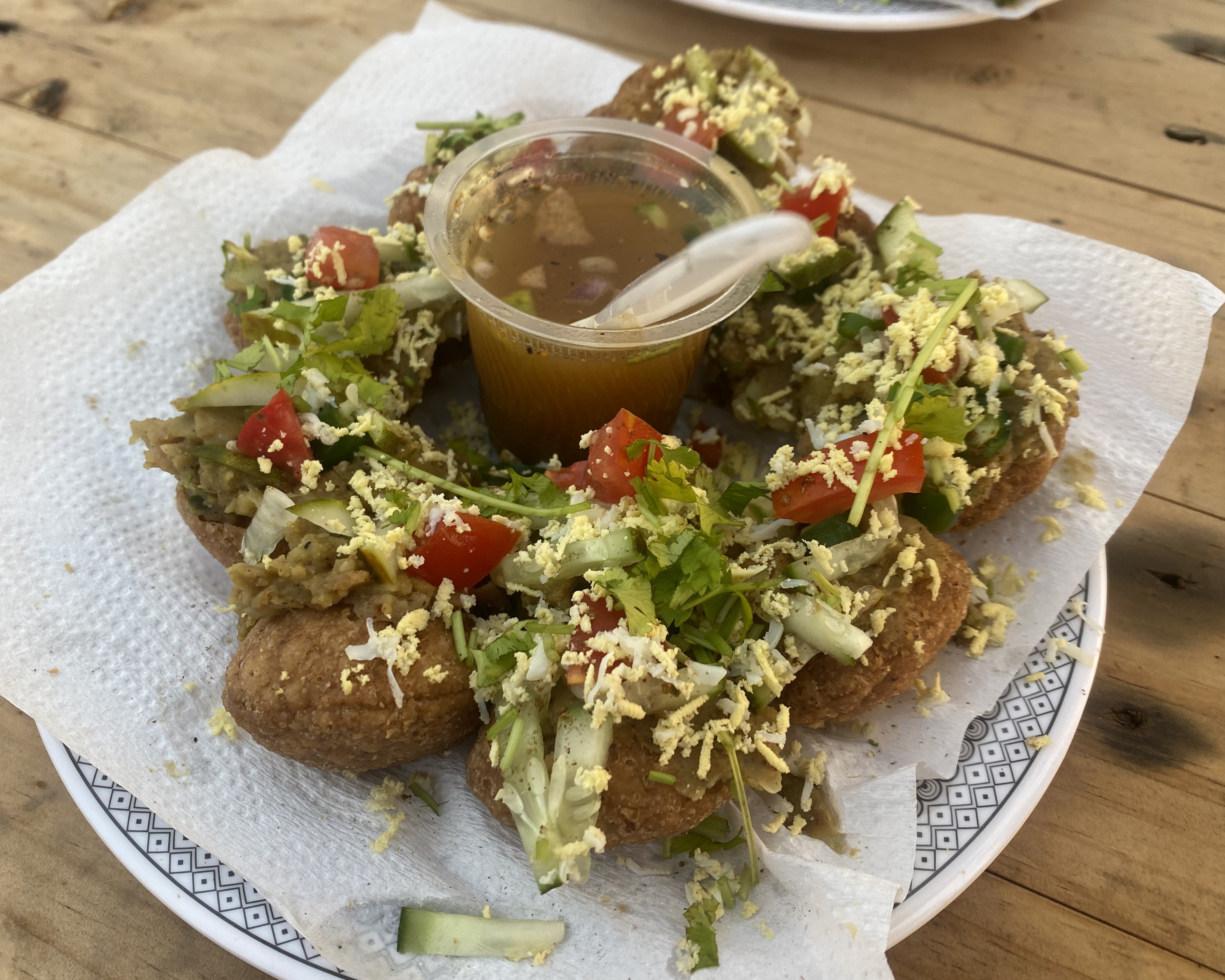 A plate of stuffed, crispy puris topped with vegetables and cheese, surrounding a cup of tamarind sauce. Vibrant, inviting, and ready to eat.