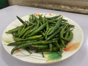 
A plate filled with fresh green chilies, varying in length and thickness. 