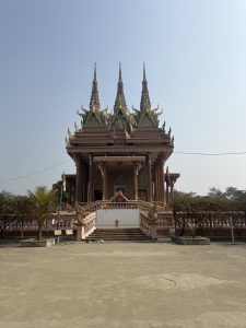 
A beautifully ornate temple stands against a clear blue sky, showcasing intricate architecture with three prominent spires topped by decorative elements. 