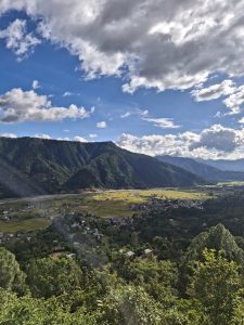 A panoramic view of a lush green valley surrounded by mountains under a partly cloudy sky.