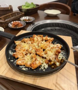 
A sizzling hot plate of cheesy chicken sits on a wooden serving board. 