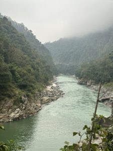 A winding river flows through a lush, green landscape, flanked by steep, rocky hills covered in dense vegetation.
