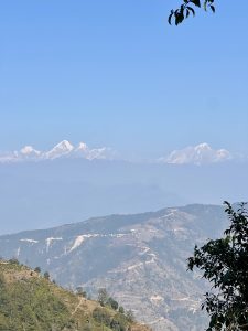 Mountains rising above rolling hills, with newly dug roads visible below on a clear winter day in Nepal.
