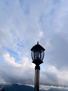 The top of a street lamp on a post, set against a a partly cloudy sky.