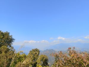A panoramic view of a mountain range under a clear blue sky, featuring snow-capped peaks in the distance. 