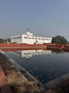 A white building with a gold spire is visible in the background, reflecting in a calm body of water in the foreground.
