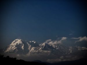 A panoramic view of majestic snow-capped mountains under a deep blue sky. Wispy clouds drift around the peaks, creating a serene and tranquil atmosphere. 