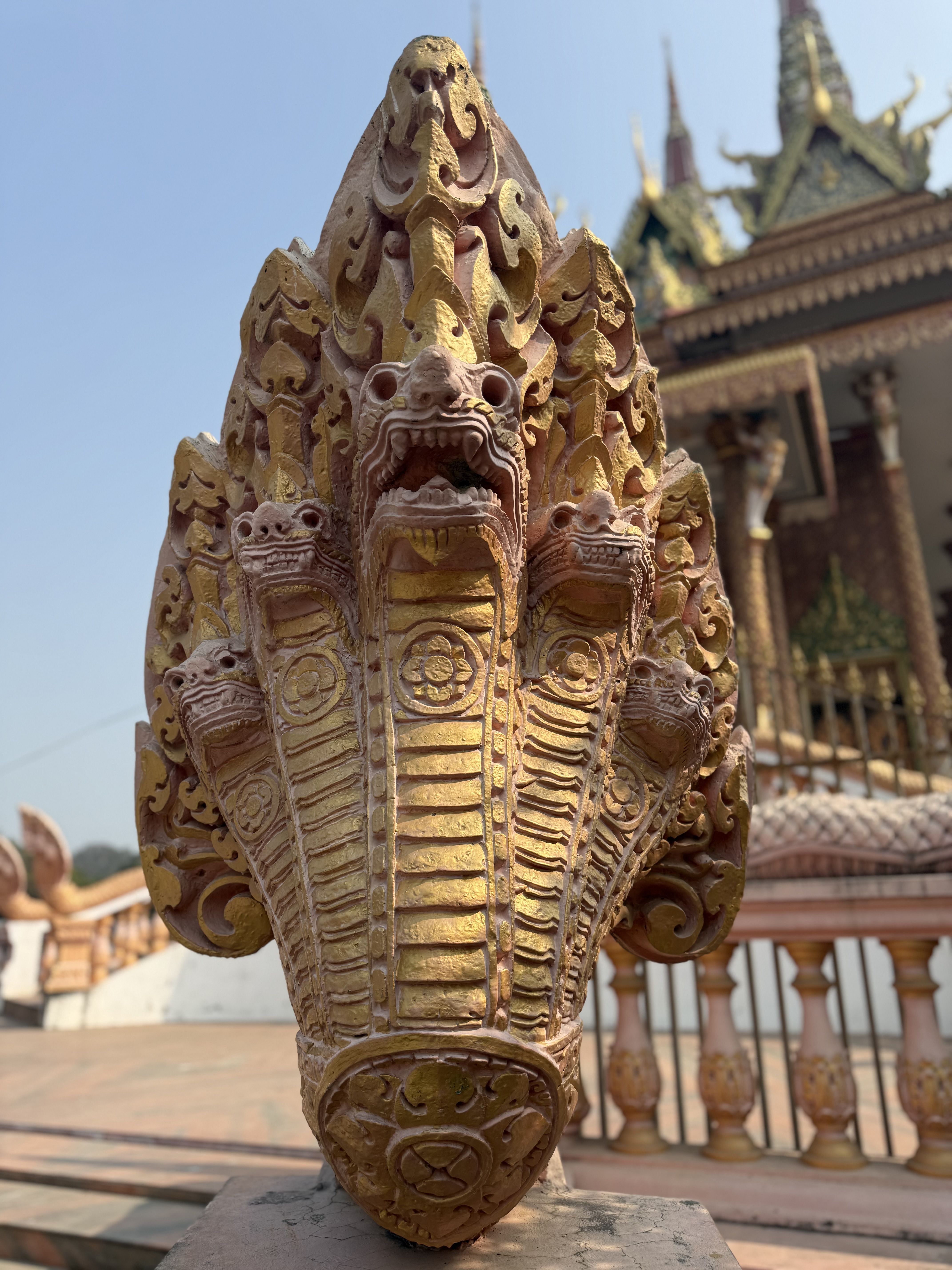 A detailed close-up of a strikingly ornate sculpture resembling a mythica Naga, adorned with intricate carvings and painted in rich gold and rosy hues