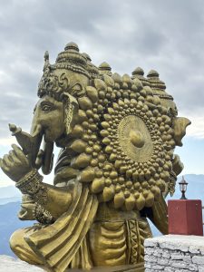 A big golden statue of Ganesha with mountains and clouds behind it.