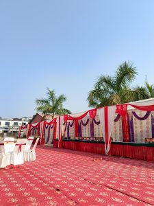 A decorated outdoor event space featuring rows of white chairs with covers, set against a vibrant patterned red carpet.
