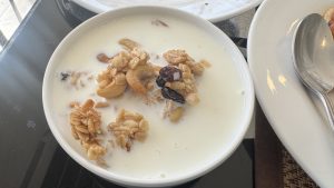 A bowl of fresh milk topped with clusters of granola, whole cashews, and dark raisins.
