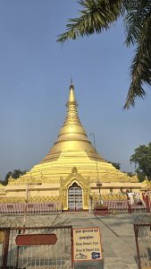 A golden stupa stands majestically against a clear blue sky, accompanied by lush green palm leaves on the left.