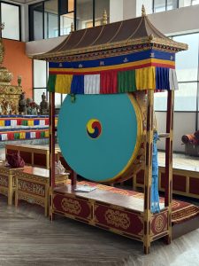 A large, ceremonial drum displayed indoors, set within an ornate wooden structure.
