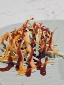 A fresh salad of cabbage, carrot, and onion drizzled with sauces on a plate in Kozhikode, Kerala, offering a colourful and crunchy side dish.
