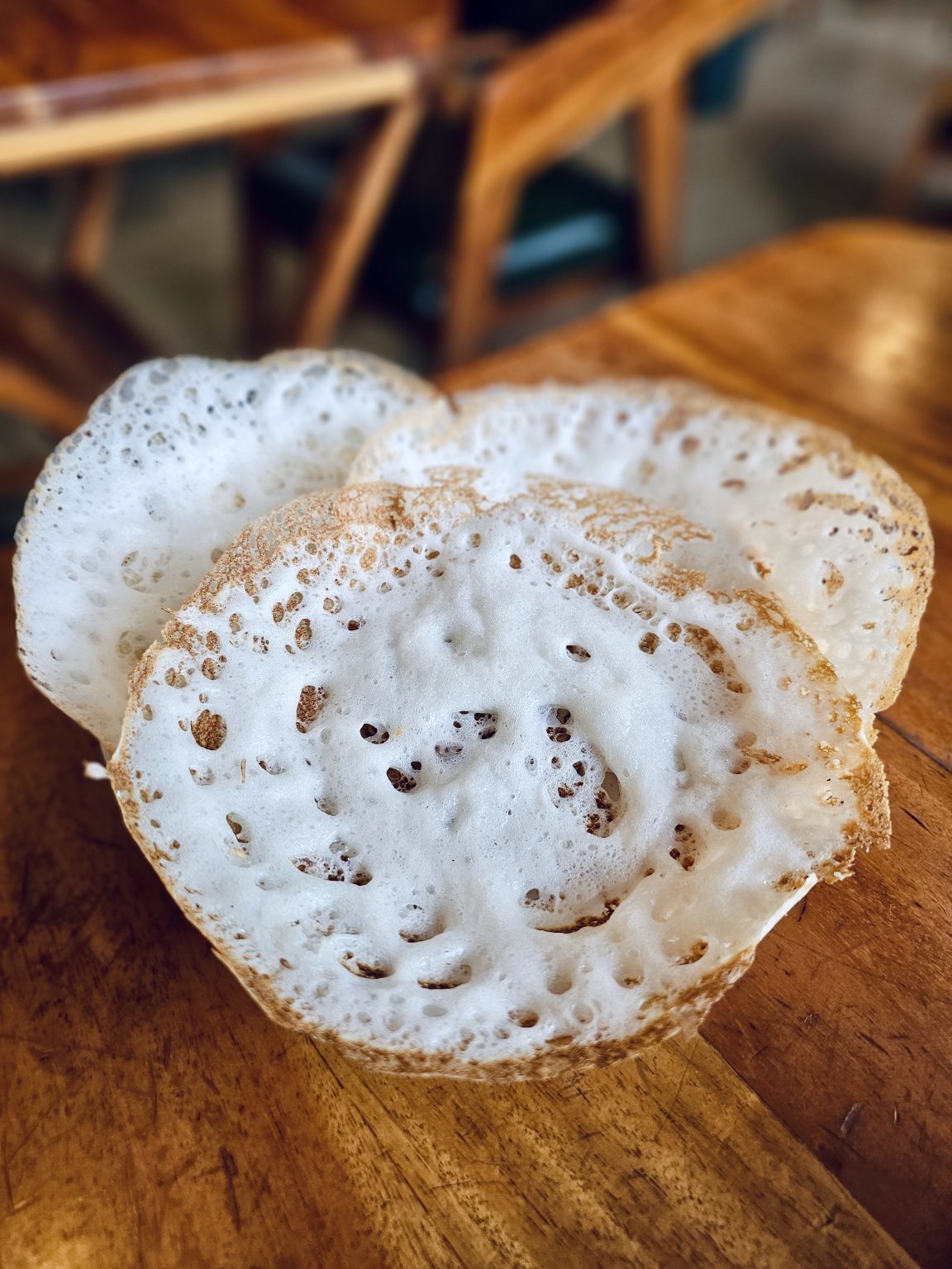 Soft, fluffy appams with crisp edges rest on a wooden table in Perumanna, Kozhikode, showing a traditional Kerala breakfast served fresh and warm.