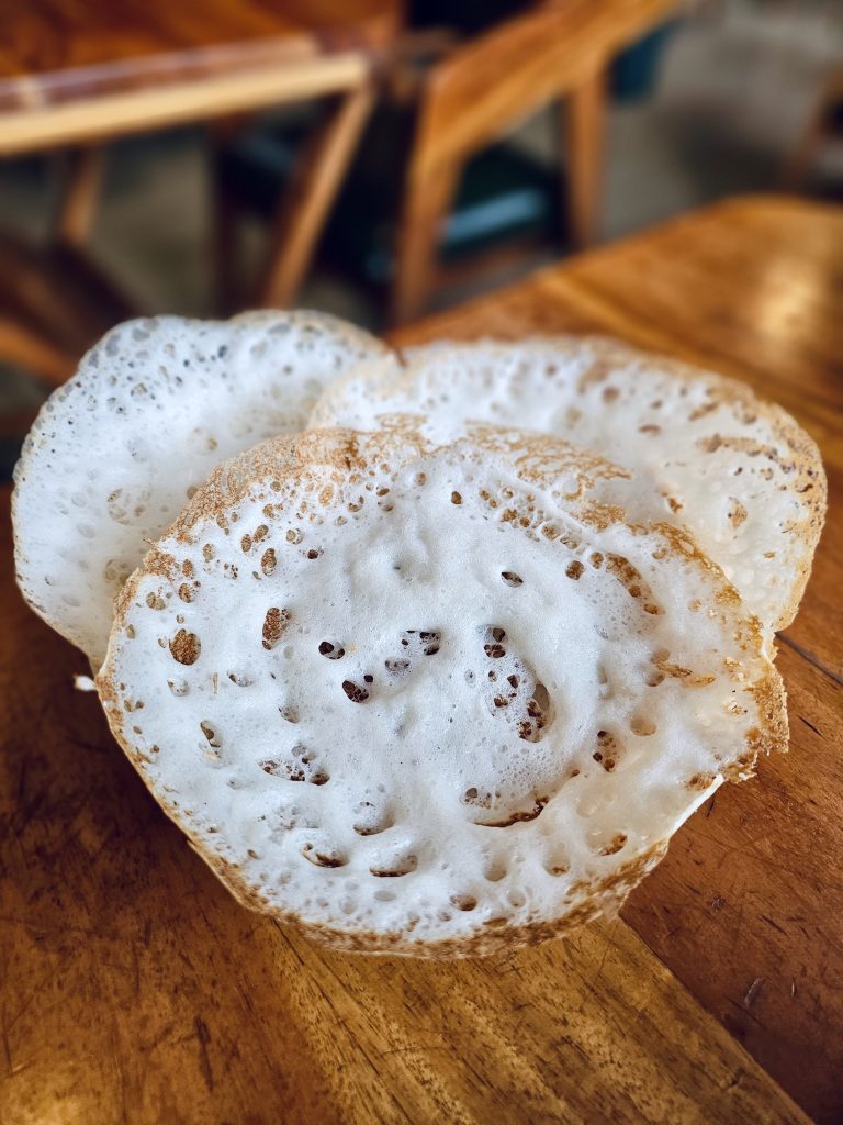 Soft, fluffy appams with crisp edges rest on a wooden table in Perumanna, Kozhikode, showing a traditional Kerala breakfast served fresh and warm.