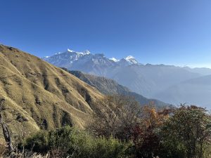 A panoramic view of majestic snow-capped mountains in the background, surrounded by rolling hills and valleys. 