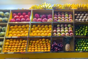 A colourful fresh fruit shelving display featuring bananas, pomegranates, dragon fruits, apples, starfruits, oranges, mangosteen, grapes, and a pineapple, creating a vibrant and fresh atmosphere.