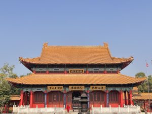 A traditional Chinese-style Lumbini temple with a curved tile roof, decorated in red and gold with detailed architectural designs.