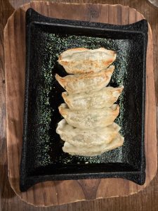 Pan-fried gyoza dumplings with lightly crisped bottoms, arranged on a black ceramic plate.