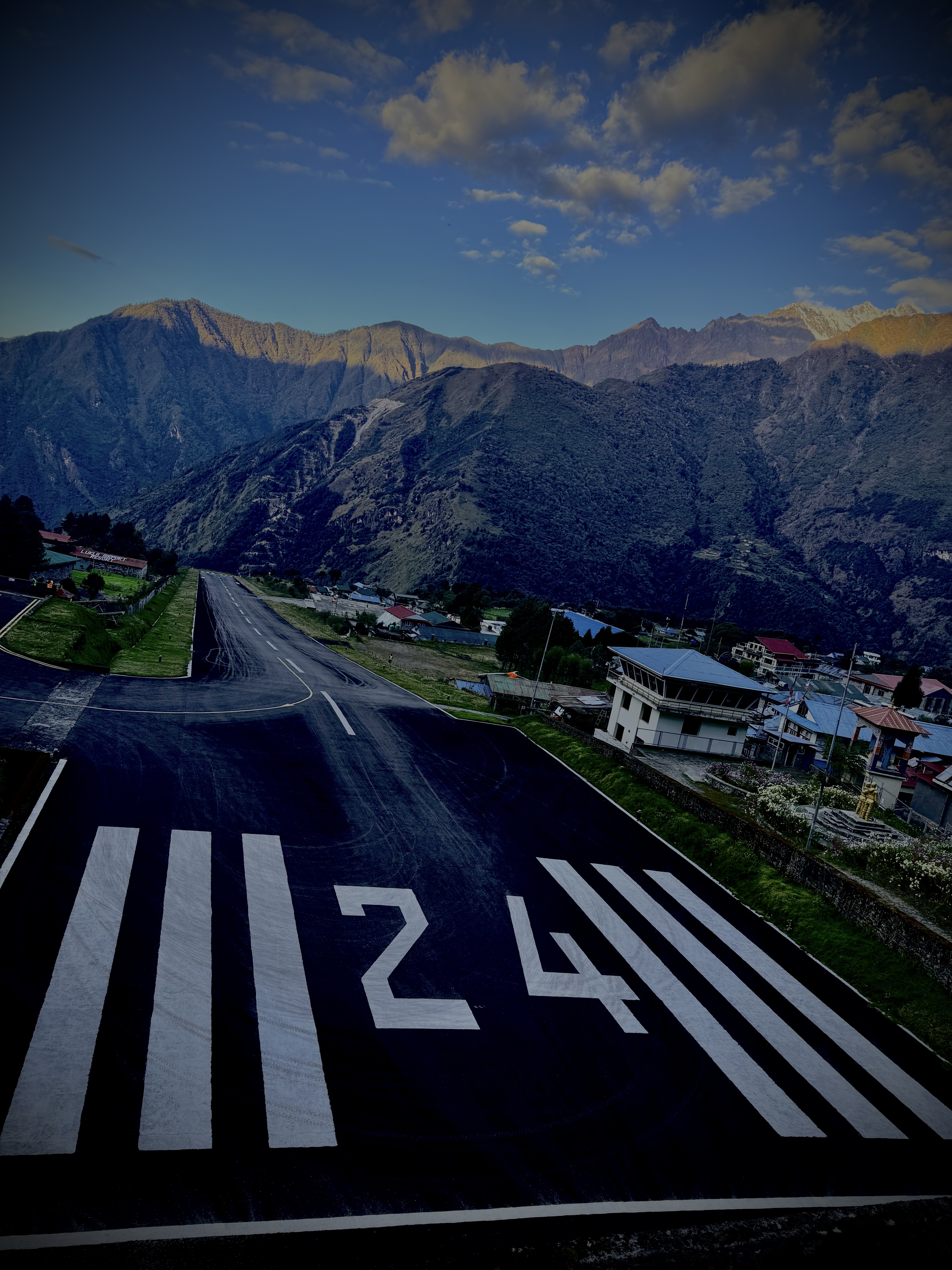 A newly paved runway stretches toward green hills and mountains under a blue sky.