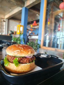 A close-up of a sesame seed-topped burger sitting on a black serving platter. 