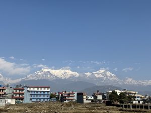 A scenic view of snow-capped mountains under a bright blue sky, with a line of colorful buildings in the foreground.