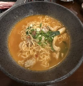 A bowl of ramen featuring yellow noodles in a rich orange broth.
