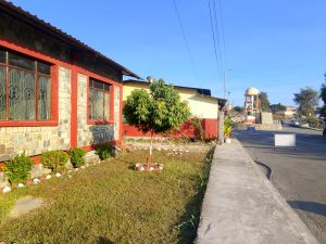 A view of a residential area featuring a stone house with red accents and large windows on the left side
